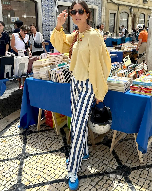 Femme portant un chemisier jaune ample et un pantalon rayé bleu et blanc sur un marché de livres en ville