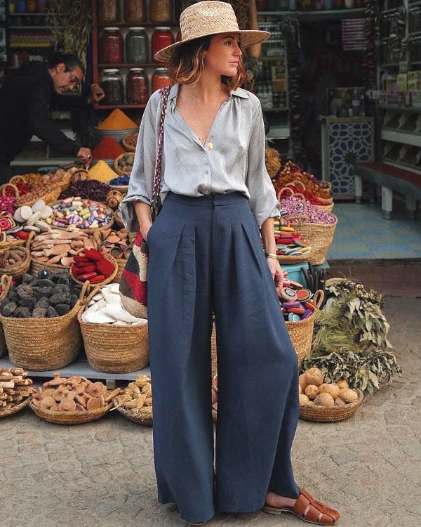 Chemise fluide bleu clair, pantalon large bleu marine, chapeau de paille et sandales en cuir sur un marché méditerranéen