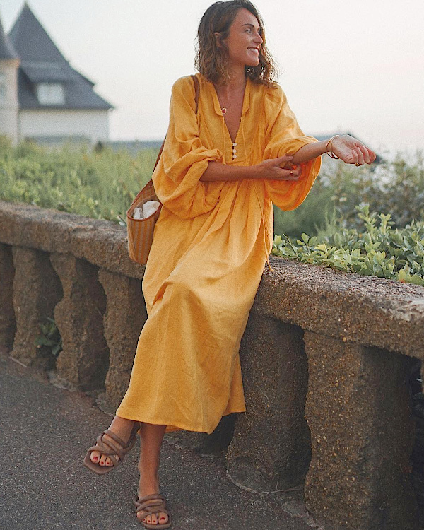 Robe longue jaune fluide, sac rayé et sandales plates portés dans une ambiance de bord de mer