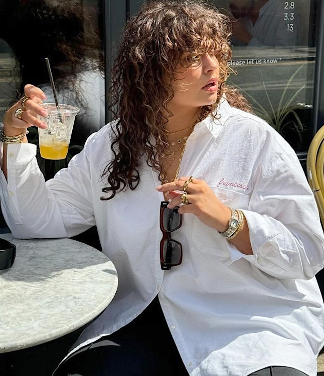 Femme ronde en chemise blanche ample avec bijoux dorés et lunettes de soleil